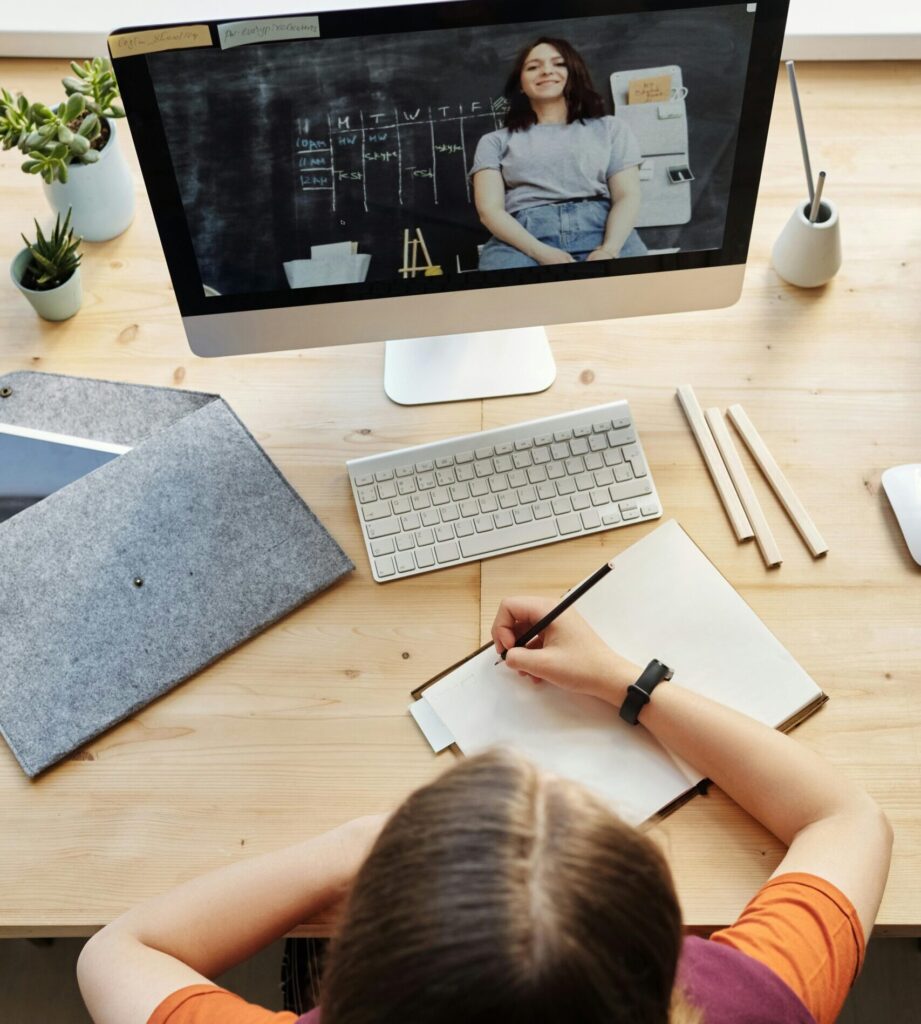 A teenage student attentively participates in a virtual classroom setting from a home office workspace.
